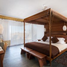 Interior view of room with double canopy bed, simple and neat decoration. Windows overlooking the environment.