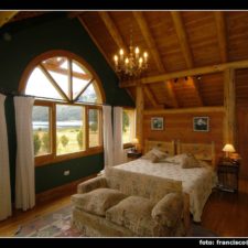 View from inside the cabin from a second floor, heated room with large double bed, high and spacious ceilings with chandelier and large windows to enjoy the view of gardens and lake.