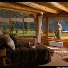 View from inside the cabin, heated room with large double bed and beautiful windows. Rustic architecture with fine wood details. Large windows overlooking the gardens and lake. Outside terrace to enjoy the surroundings.