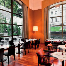 Dining room with large windows overlooking the gardens and interior facade of the hotel.