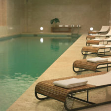 Indoor pool with elegant floors and marble walls in warm colors, with comfortable lounge chairs with a modern design.