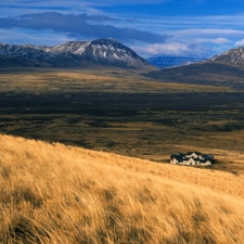 Panoramic view of the lodge in the middle of gently sloping grasslands overlooking impressive snowy mountains.