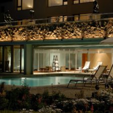 Night view from the garden to the outdoor pool and terraces. Indoor pool lounge open at night.