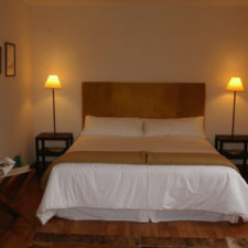 Room with a double bed, warm lighting, wooden floors, light walls and minimalist decoration.