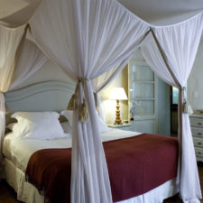 Room with double bed with white fabric canopy. Colonial style with rustic touches where the white color predominates.