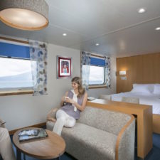 Stateroom with double bed and living room, bay windows with ocean views.