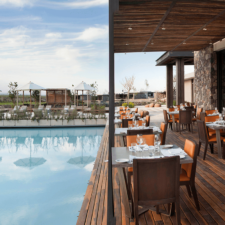 Restaurant deck terrace that adjoins a beautiful pool. Warm and woody colors, stone details and glass windows. On the horizon you can see a terrace and the landscape with pastures.