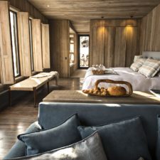 Interior of a room with a double bed. Rustic wooden architecture with windows and views of the snowy mountains.